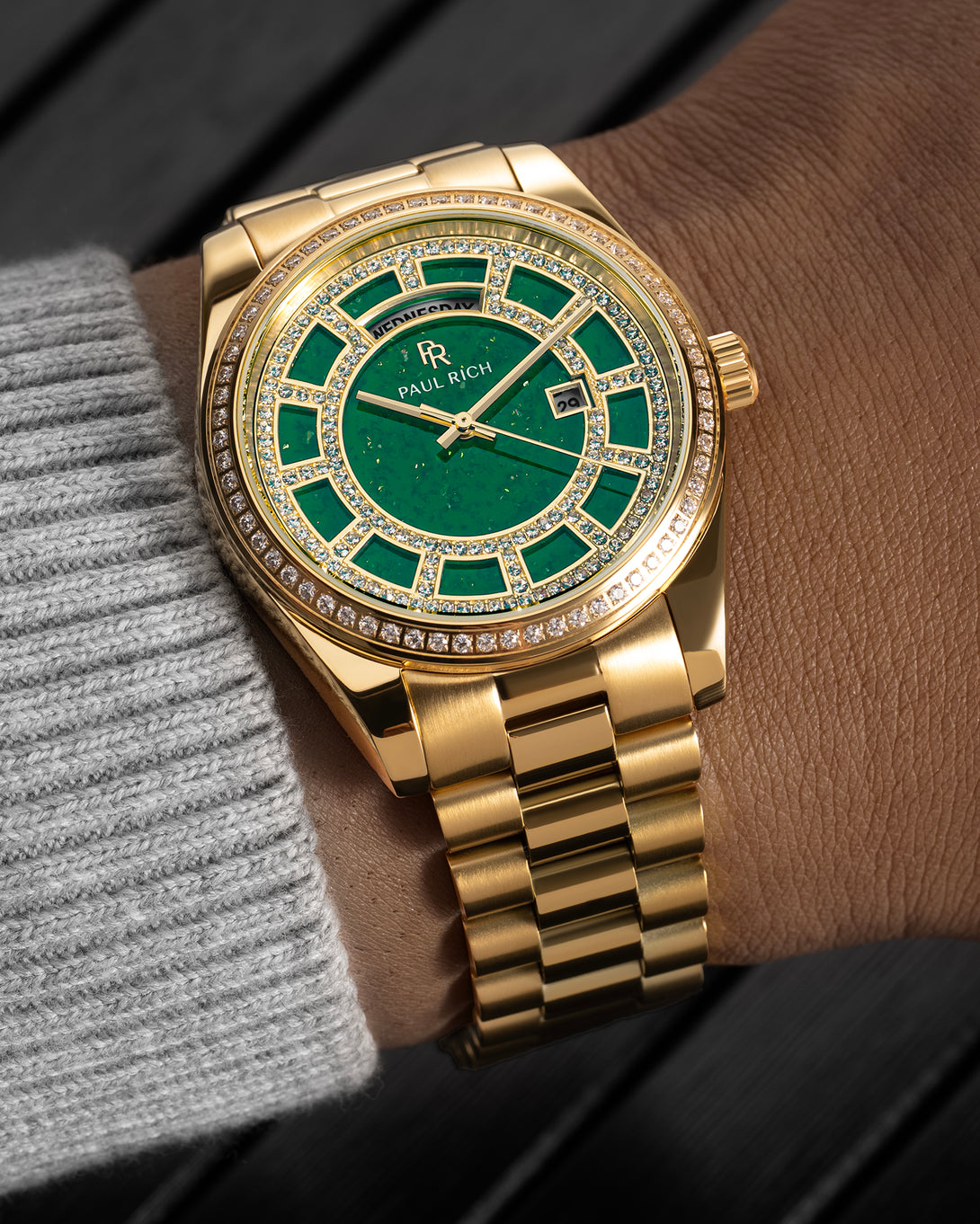 Gold watch with a green aventurine dial, pavé diamond bezel, and day–date display shown on a wrist with a matching gold bracelet. Gold watch with a green aventurine dial, pavé diamond bezel, and day–date display shown on a wrist with a matching gold bracelet.