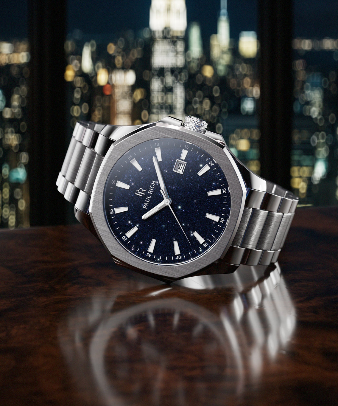 Paul Rich watch with brushed silver case and blue aventurine dial resting on dark wood surface, with NYC skyline at night in background. product_visual Paul Rich watch with brushed silver case and blue aventurine dial resting on dark wood surface, with NYC skyline at night in background. product_visual