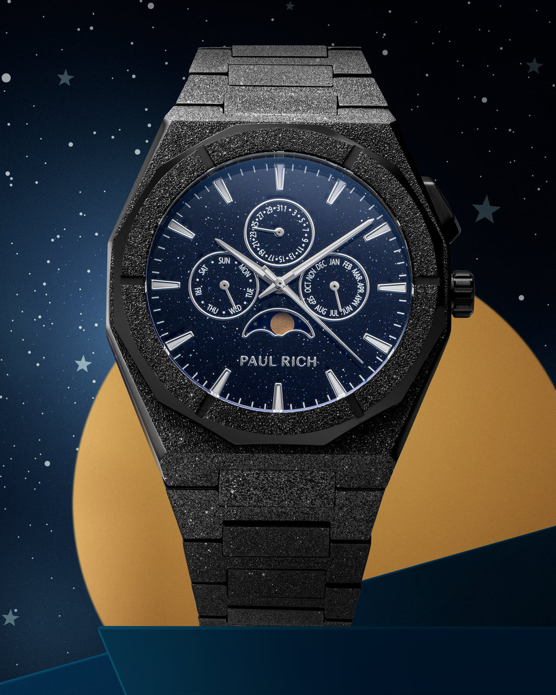 Frosted black stainless steel watch with blue aventurine dial, moonphase, and subdials, set against a starry night sky and gold circle backdrop. product_visual