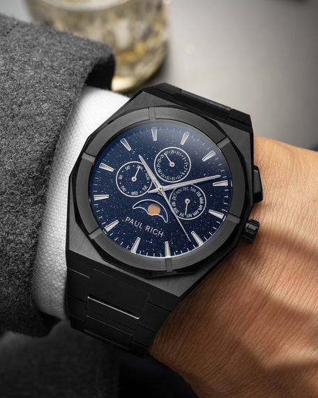 Brushed black moonphase watch on wrist with aventurine dial, calendar subdials, and black steel bracelet. product_visual, [lifestyle]