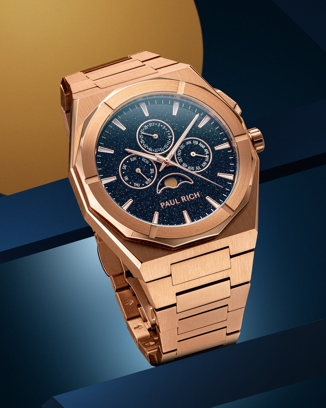 Rose gold-tone stainless steel watch with blue aventurine dial, moonphase, and subdials, displayed on a geometric blue and gold backdrop. product_visual