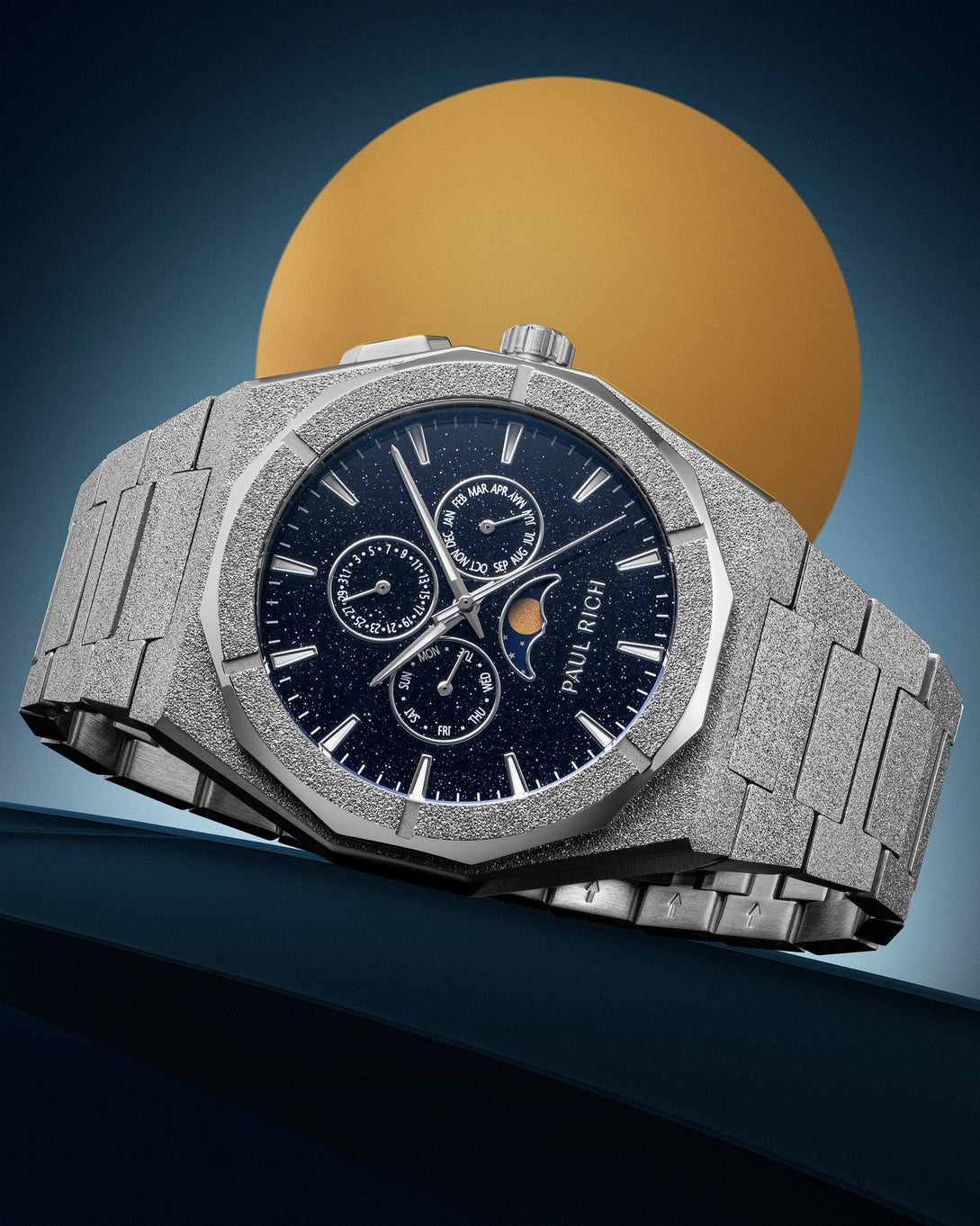 Frosted silver stainless steel watch with blue aventurine dial, moonphase, and subdials, displayed against a blue backdrop with a gold circle. product_visual