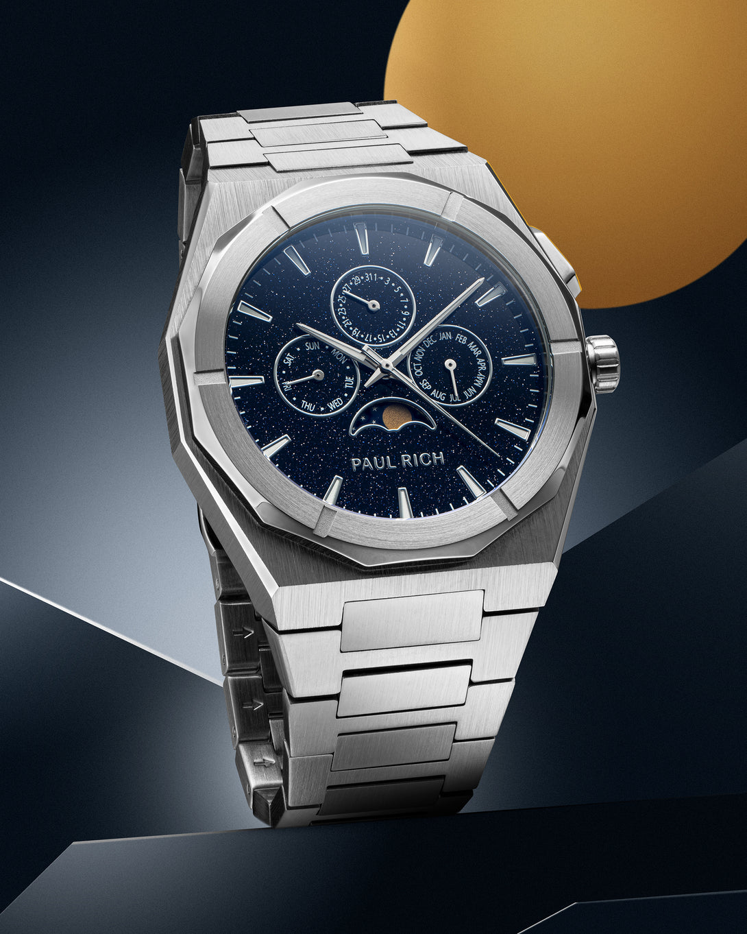 Silver stainless steel watch with blue aventurine dial, moonphase, and subdials, displayed on a geometric silver and blue backdrop with a gold circle. product_visual
