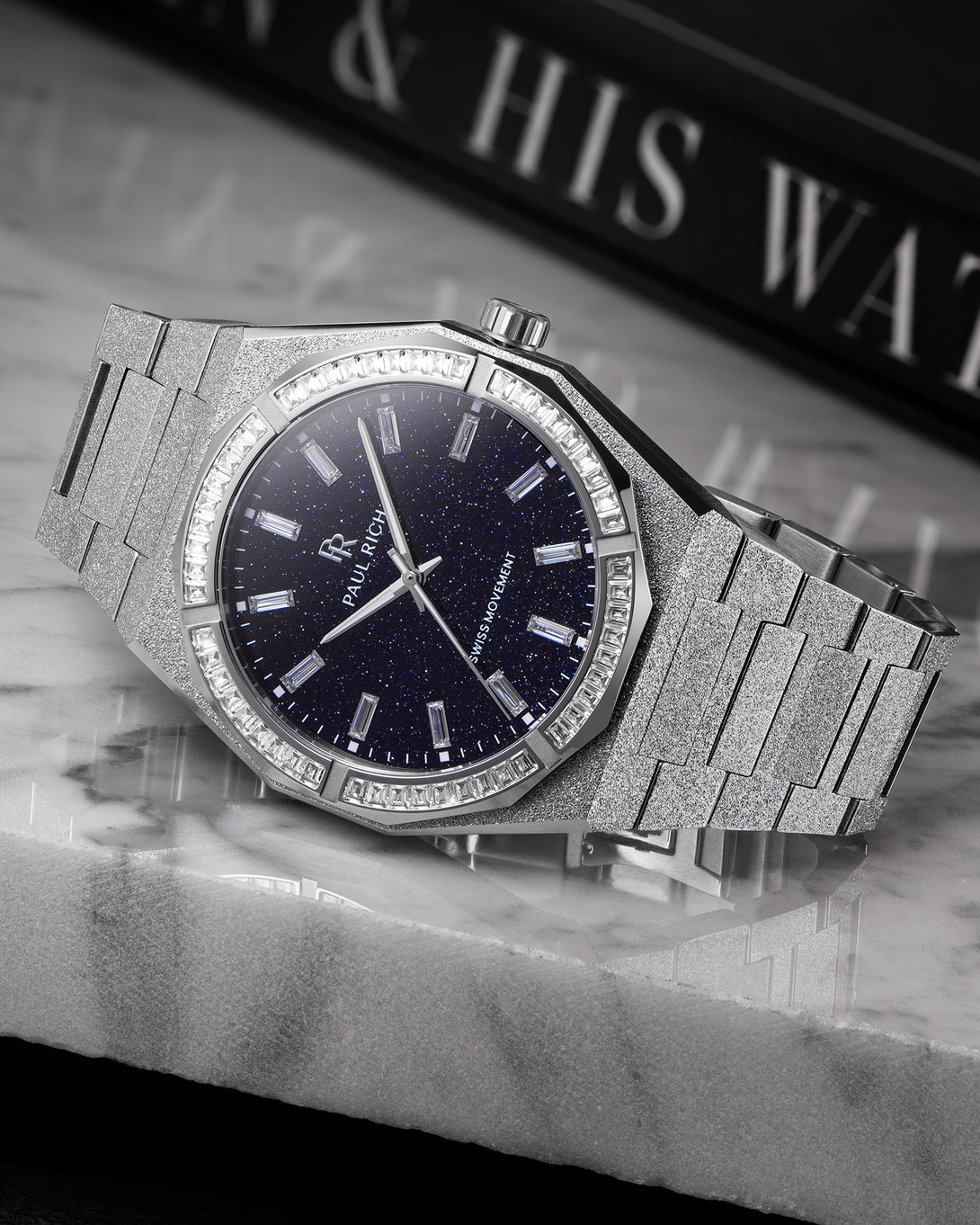 Silver frosted watch with aventurine dial and baguette-cut moissanite bezel, displayed on a polished marble surface. product_visual, Quartz I Automatic