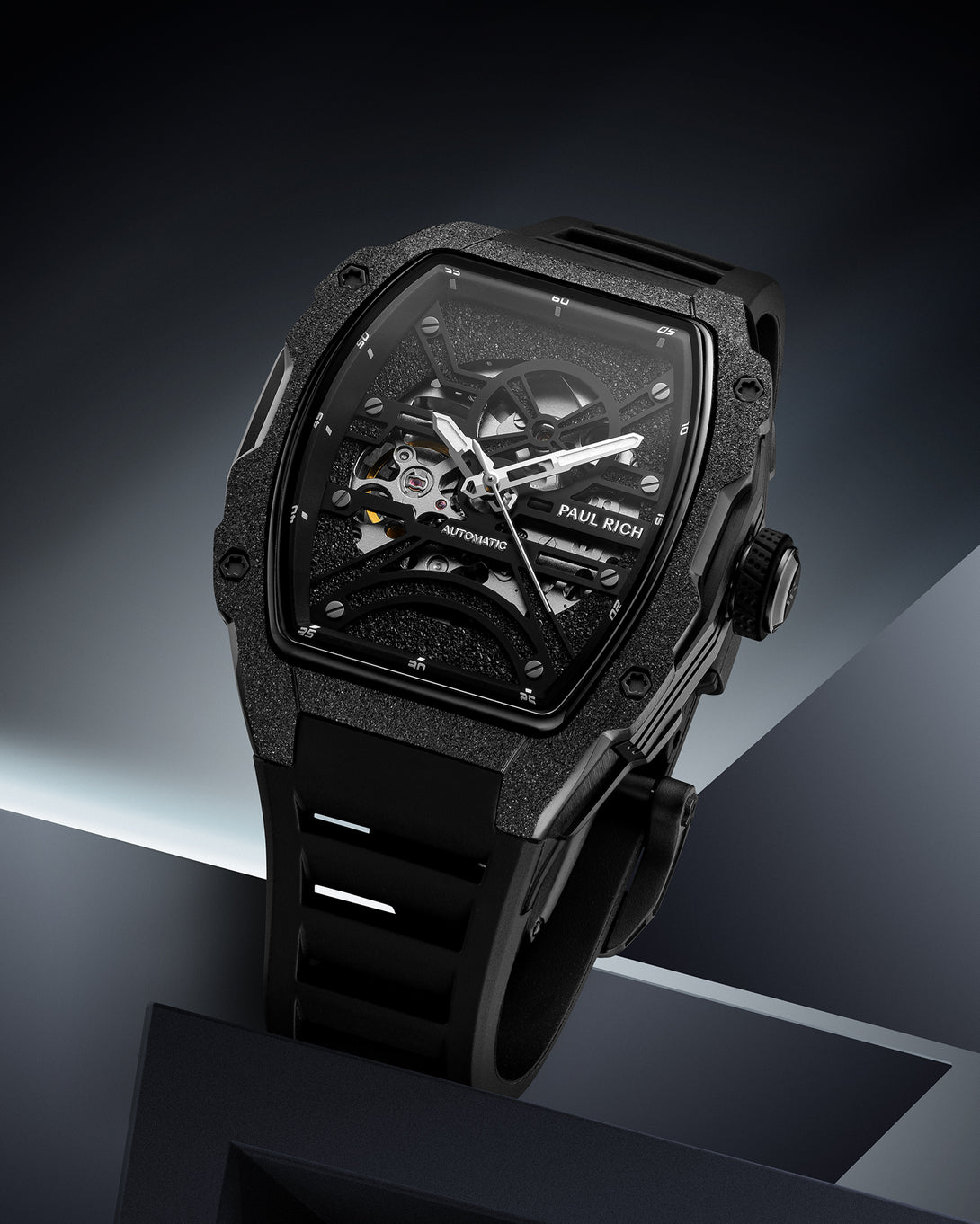 Black frosted tonneau case watch with open skeleton dial and black strap on a dark geometric background. product_visual