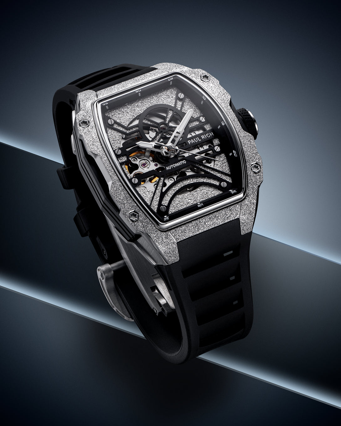 Silver frosted tonneau case watch with open skeleton dial and black strap on a dark blue geometric background. [product_visual]
