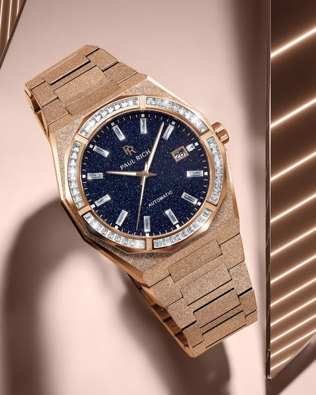 Rose gold Paul Rich watch with frosted texture, blue aventurine dial, and gem-set bezel, resting on a peach-toned reflective surface. product_visual, [lifestyle] Quartz | Automatic