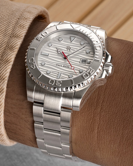 Stainless steel watch with a white wave-textured dial and red seconds hand shown on a wrist, highlighting the bezel, bracelet, and brushed finish. [lifestyle] product_visual