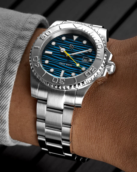 Stainless steel watch with a blue wave-textured dial and yellow seconds hand shown on a wrist, highlighting the bezel, markers, and brushed bracelet. [lifestyle] product_visual