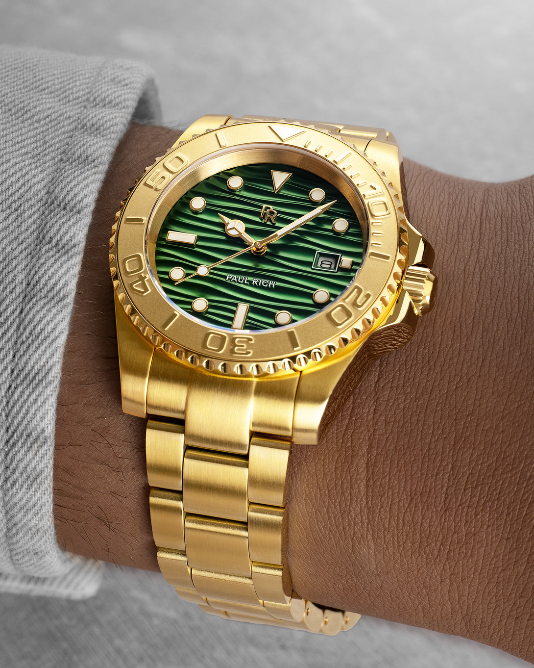 Gold-tone stainless steel watch with a green wave-textured dial shown on a wrist, highlighting the bracelet, bezel, and luminous markers. [lifestyle] product_visual
