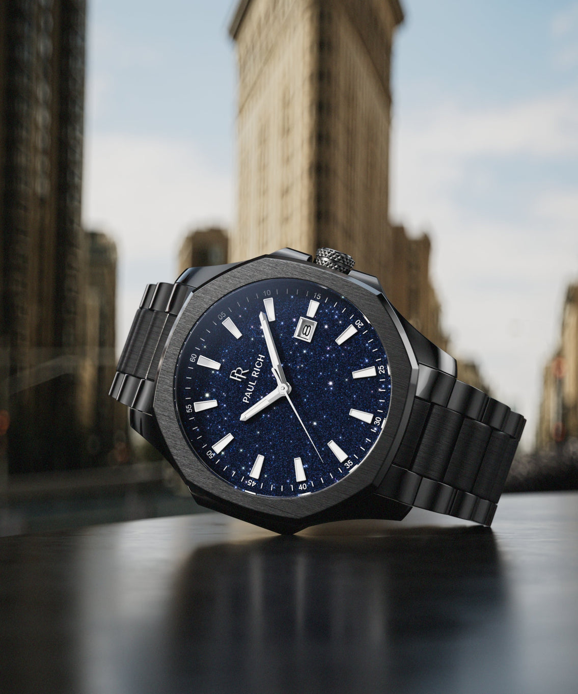 Paul Rich watch with brushed black case and blue aventurine dial displayed on a table in front of the Flatiron Building in New York City. product_visual