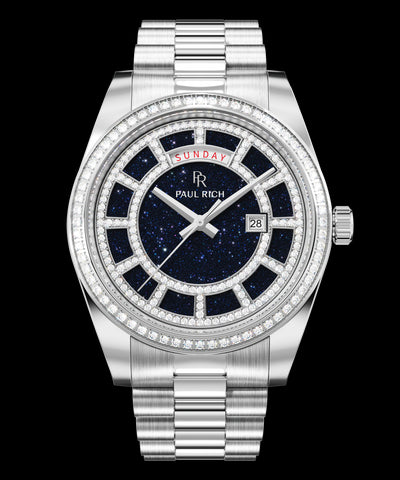 Silver watch with a blue aventurine dial, day and date windows, and a bezel and hour markers set with clear stones on a full stainless-steel bracelet.