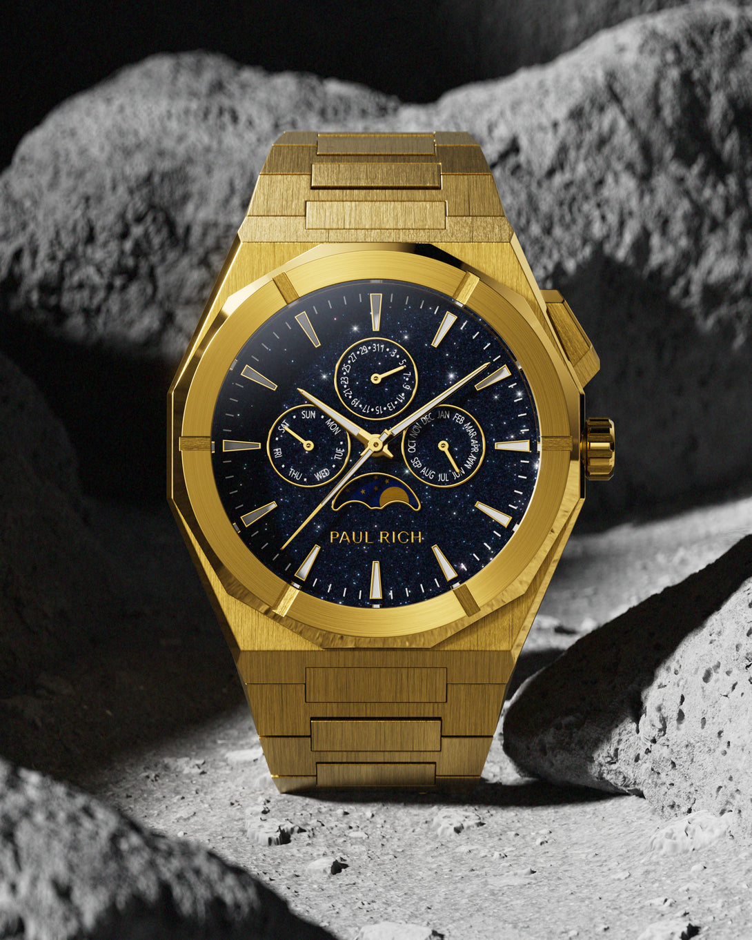 Brushed gold stainless steel watch with blue aventurine dial, moonphase, and subdials, displayed against a rugged grey lunar rock background. product_visual