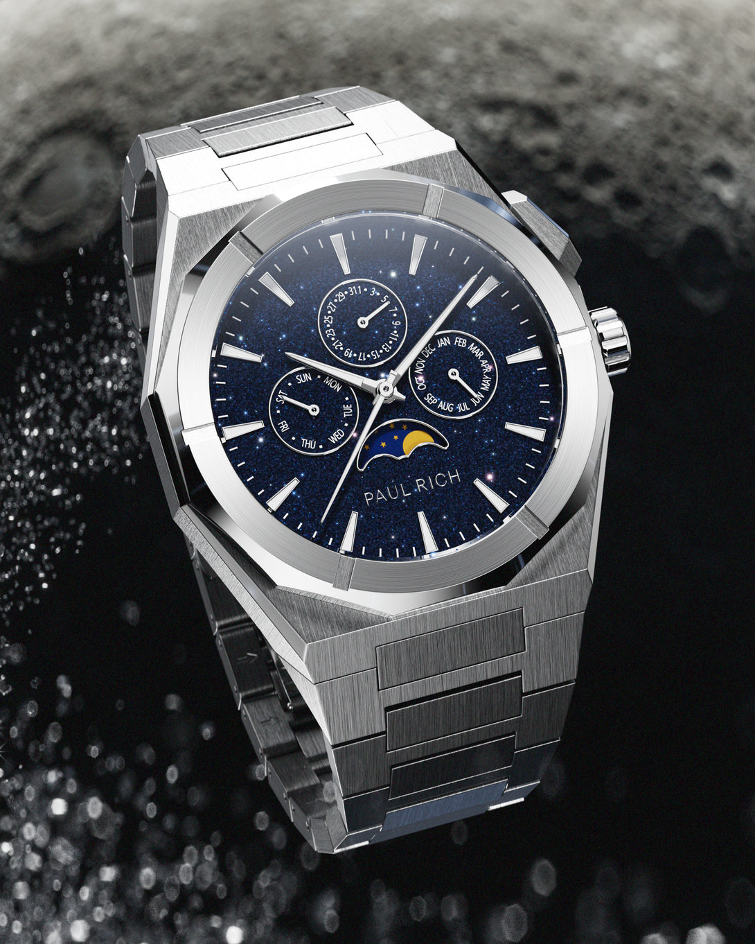 Brushed silver stainless steel watch with blue aventurine dial, moonphase, and subdials, displayed against a textured black and grey lunar surface backdrop. product_visual